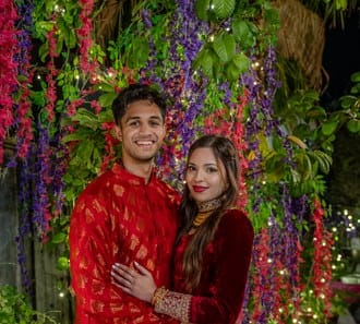 South Asian couple in red and gold wedding attire among flowers