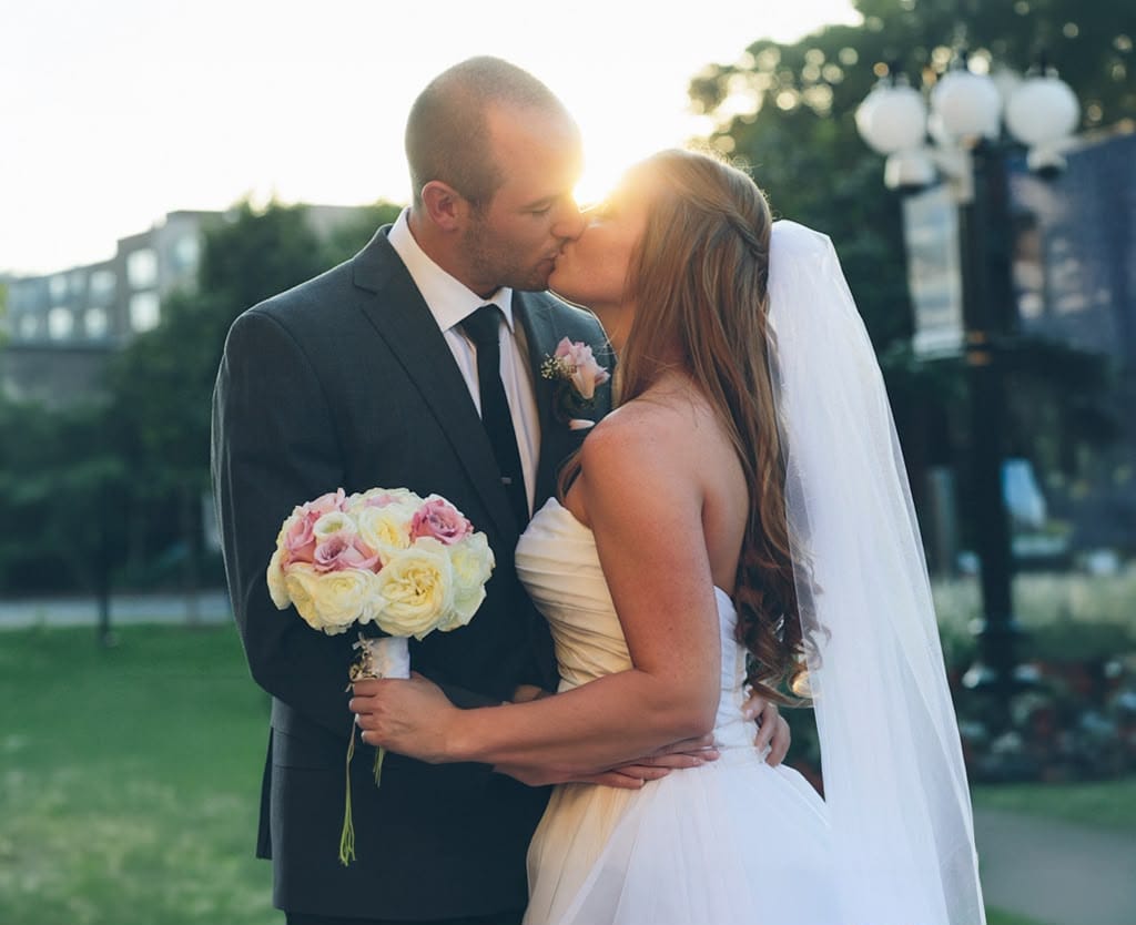 Bride and groom kissing at sunset with a rose bouquet